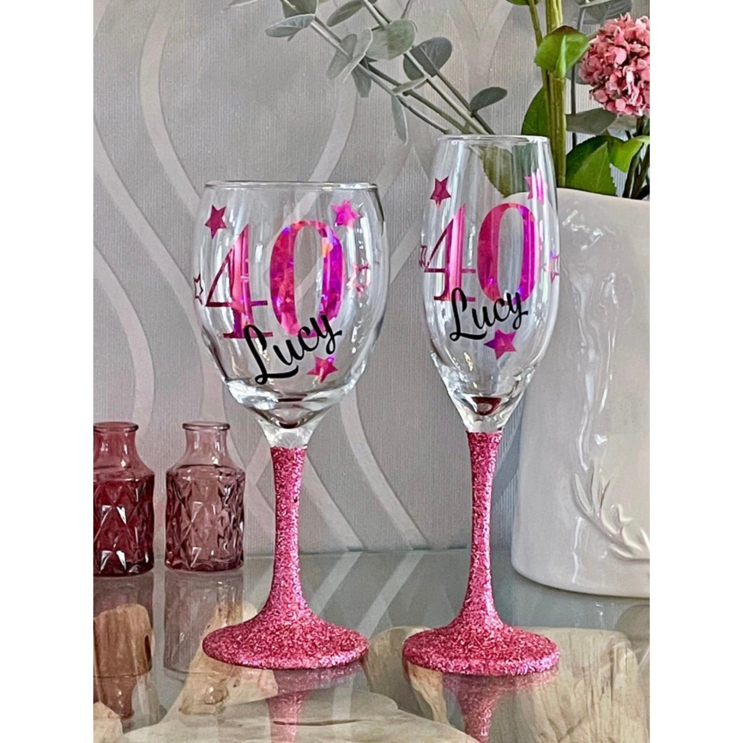 Personalised glitter-bottomed glass with decorative star design β custom name and age gift. Hand-applied glitter base, sealed for sparkle, available in gold, silver, rose gold and more. Choice of gin glass, wine glass, shot glass or matching lit wine bottle. Unique keepsake for birthdays, celebrations or special occasions. Gift-wrapped with optional personalised tote bag.