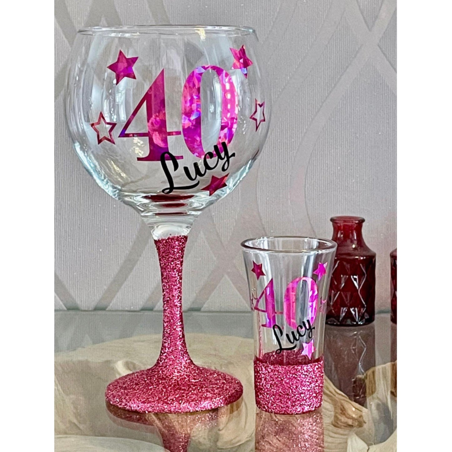 Personalised glitter-bottomed glass with decorative star design β custom name and age gift. Hand-applied glitter base, sealed for sparkle, available in gold, silver, rose gold and more. Choice of gin glass, wine glass, shot glass or matching lit wine bottle. Unique keepsake for birthdays, celebrations or special occasions. Gift-wrapped with optional personalised tote bag.