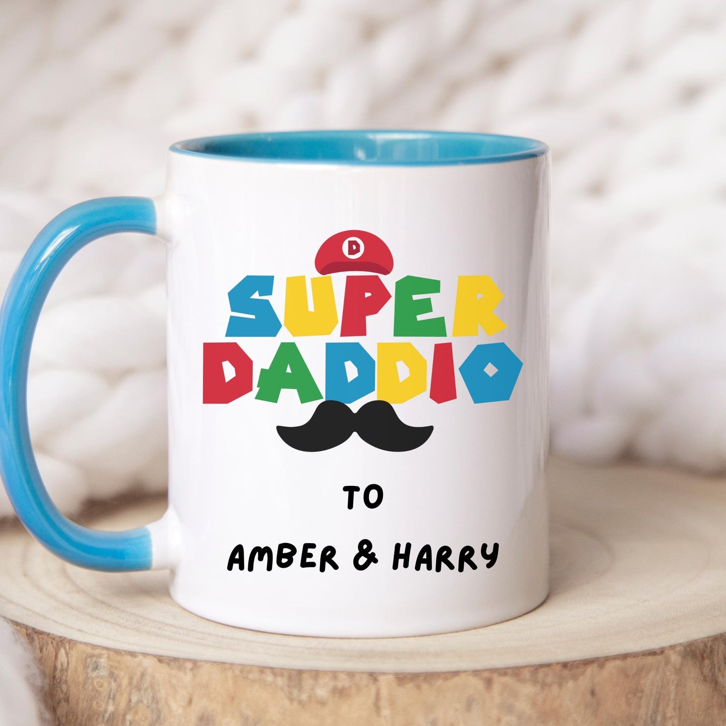White ceramic coffee mug with colorful text reading 'Super Daddio', a red Mario-style hat, black moustache graphic, and personalised 'To Amber & Harry' message โ perfect custom Father's Day gift for gamer dads.