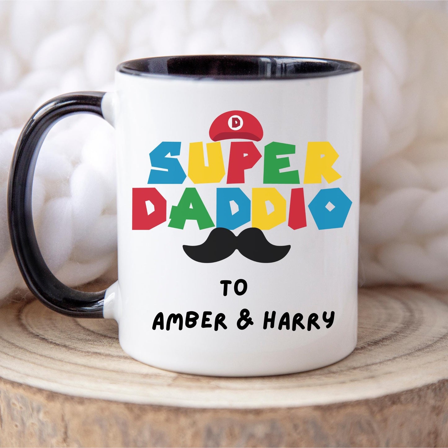 White ceramic coffee mug with colorful text reading 'Super Daddio', a red Mario-style hat, black moustache graphic, and personalised 'To Amber & Harry' message โ perfect custom Father's Day gift for gamer dads.