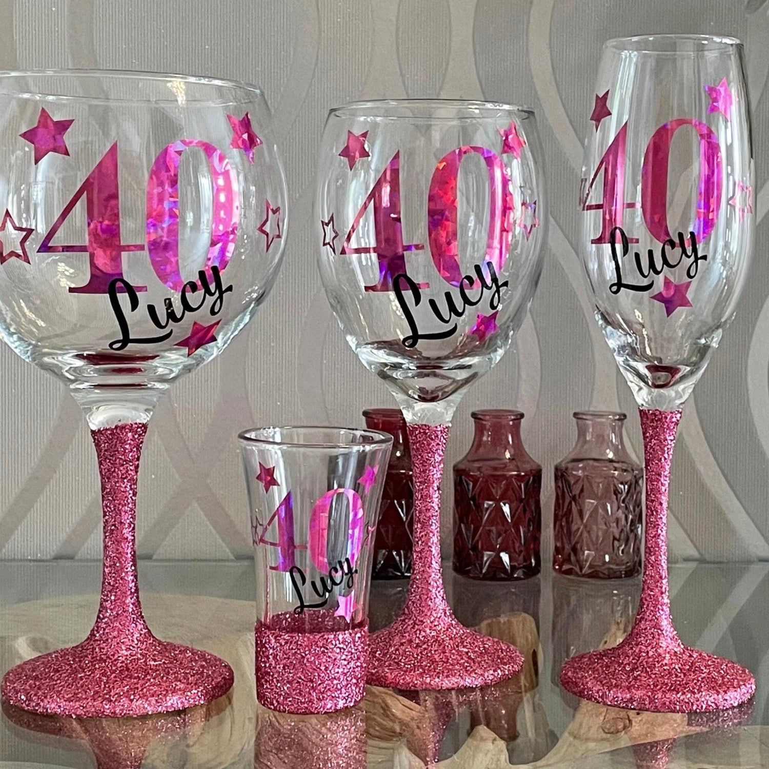 Personalised glitter-bottomed glass with decorative star design — custom name and age gift. Hand-applied glitter base, sealed for sparkle, available in gold, silver, rose gold and more. Choice of gin glass, wine glass, shot glass or matching lit wine bottle. Unique keepsake for birthdays, celebrations or special occasions. Gift-wrapped with optional personalised tote bag.