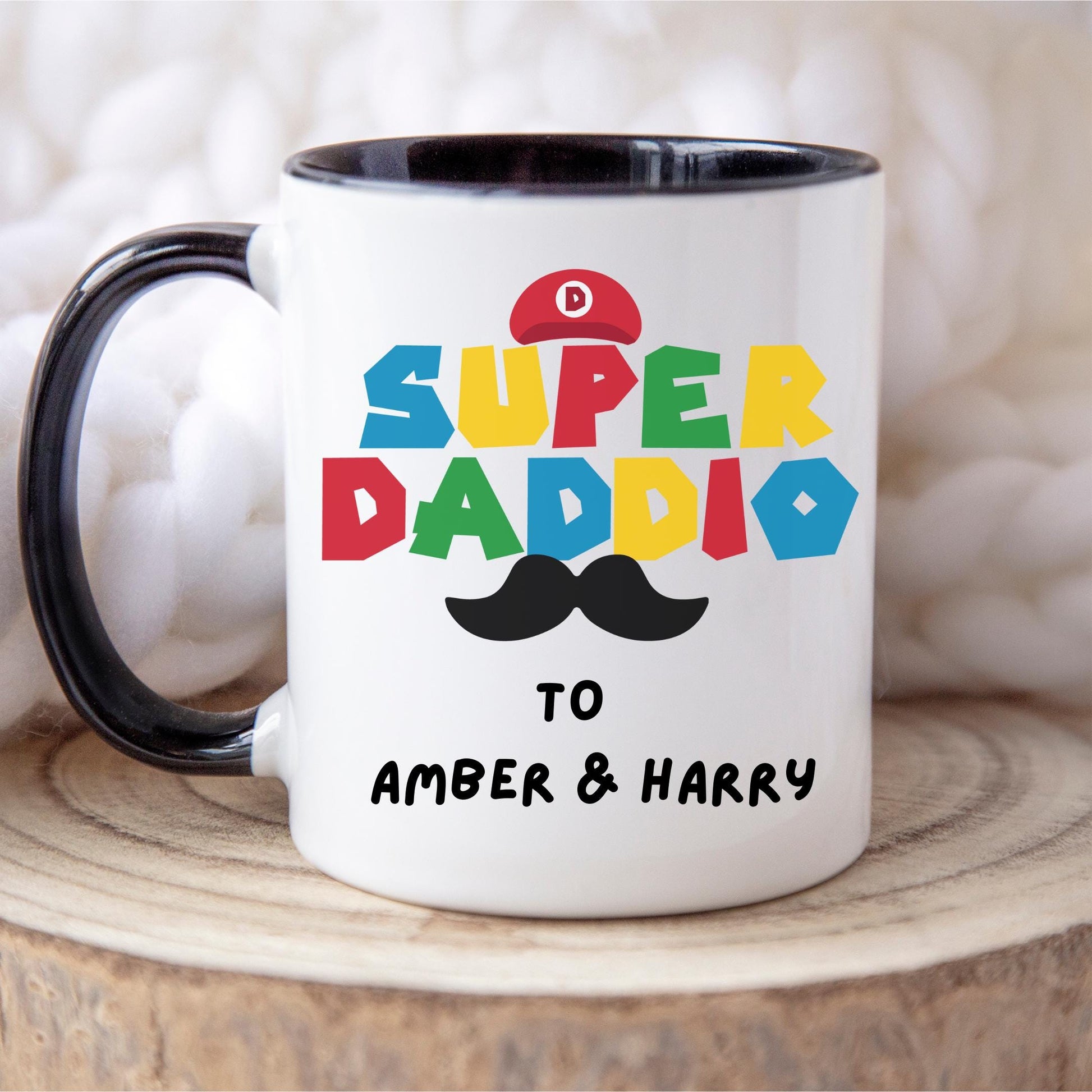White ceramic coffee mug with colorful text reading &#39;Super Daddio&#39;, a red Mario-style hat, black moustache graphic, and personalised &#39;To Amber & Harry&#39; message – perfect custom Father&#39;s Day gift for gamer dads.